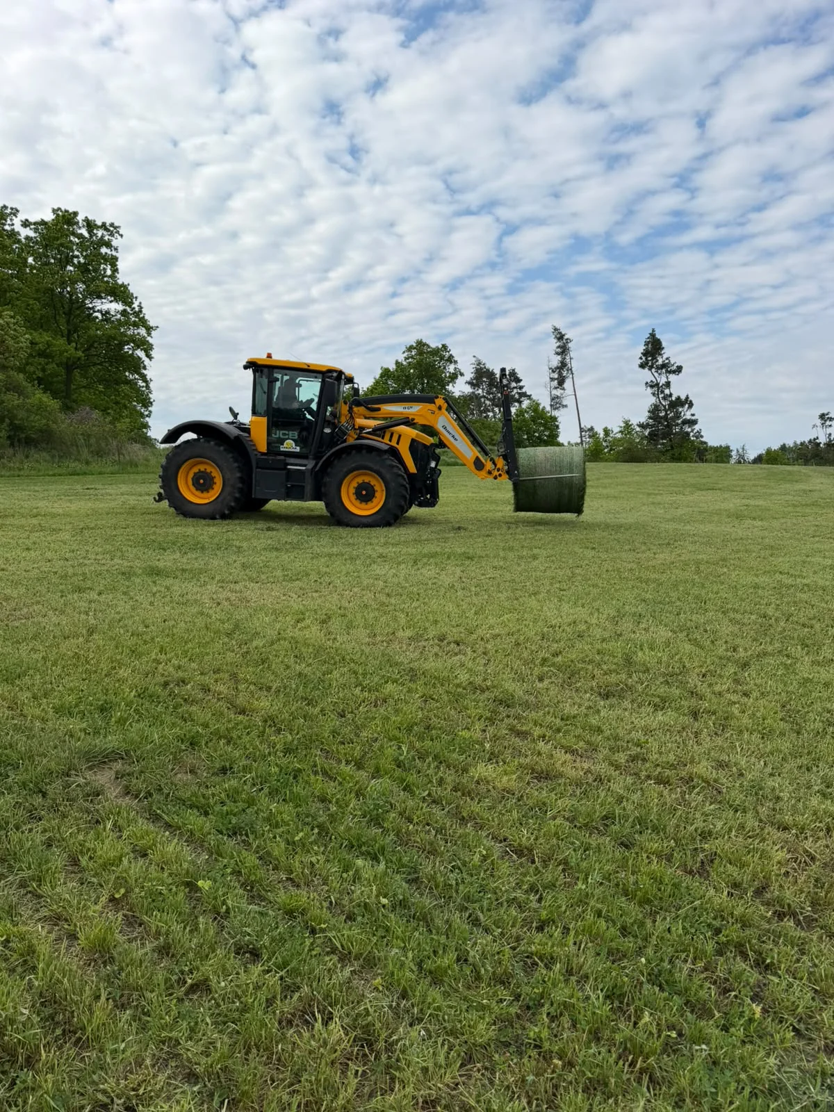 Traktor JCB s balíkem senáže na louce